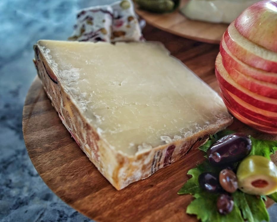 Slice of mature Cantal cheese on platter with apple and olives