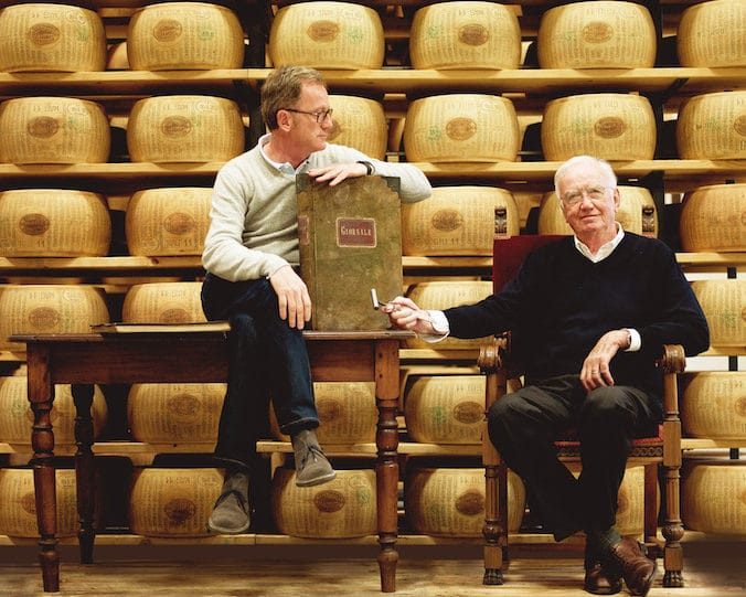 2 generations of Cravero men in front of wheels of Parmigiano Reggiano