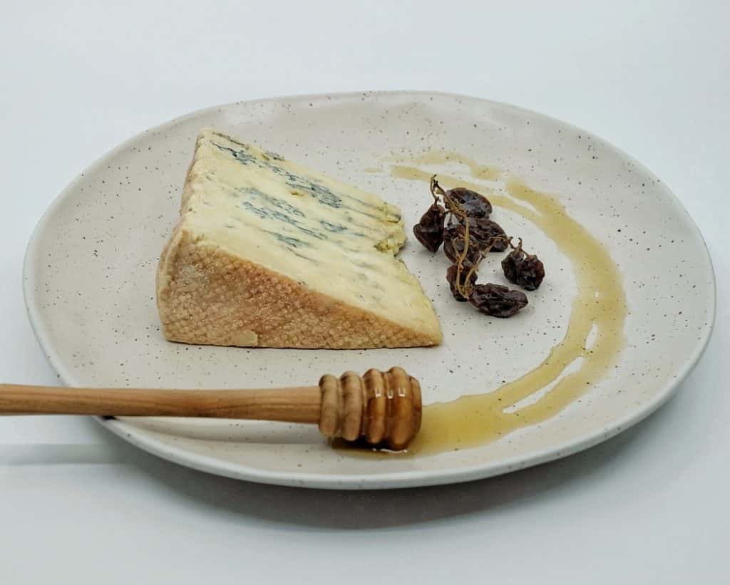 Slice of Oak Blue cheese on plate with honey and muscatels