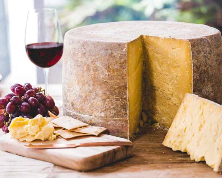 Large wheel of Pyengana Clothbound Cheddar with a wedge cut out served with red wine and grapes