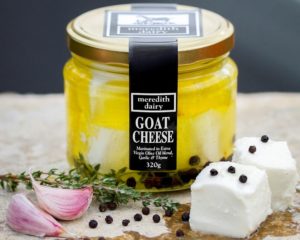 Jar of Meredith Dairy Marinated Goat Cheese on board with garlic and pepper