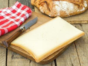 Slice of Beaufort cheese on a wooden board with knife and table cloth