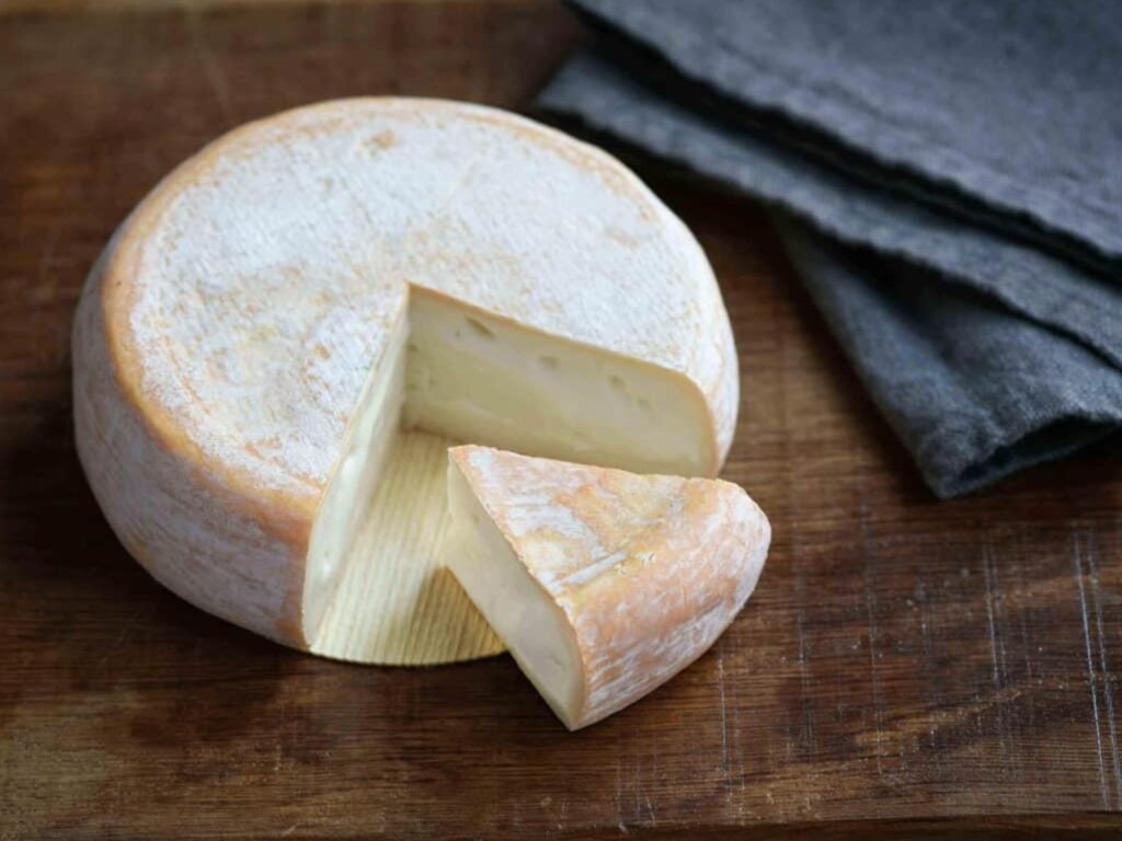 Small wheel of Chevrotin cheese on wooden table with a wedge cut out