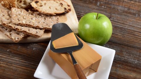 Block of Gjetost Norwegian brown cheese being sliced for a sandwich